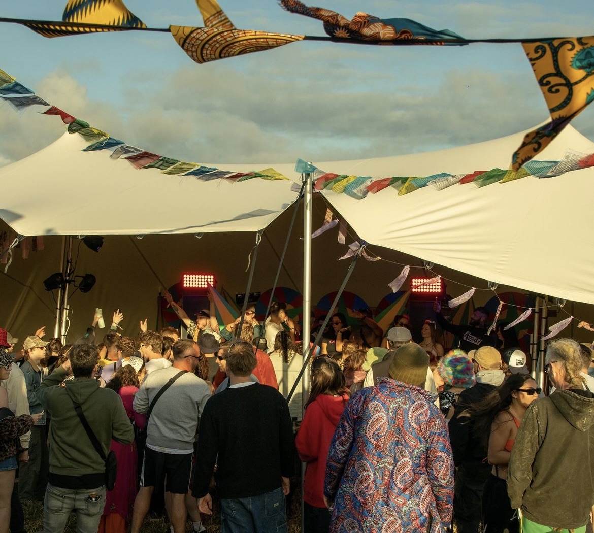 Kites and bunting strung above a festival stretch tent, crowd watching the stage