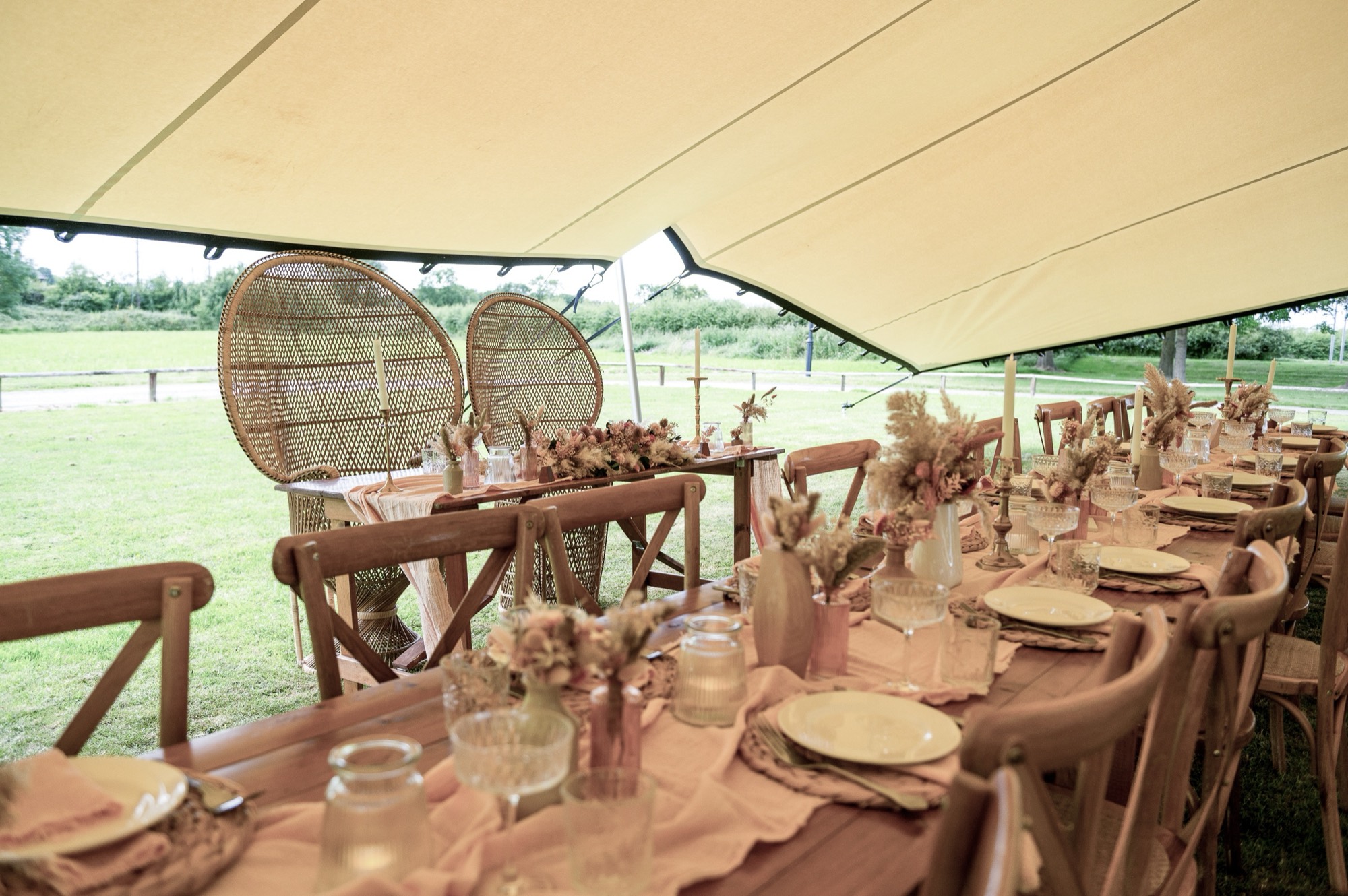Peacock chairs at the head of a dressed table under a stretch tent