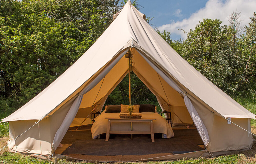 Bell tent open at the door with a double bed made up inside