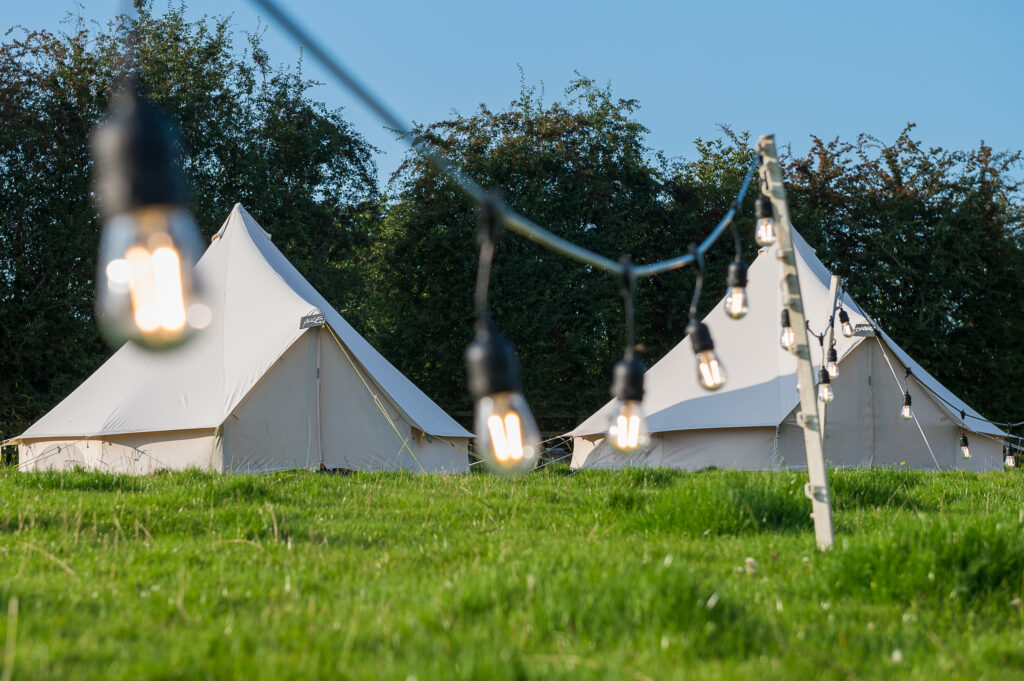 Bell tents lined up under festoon lighting at an event