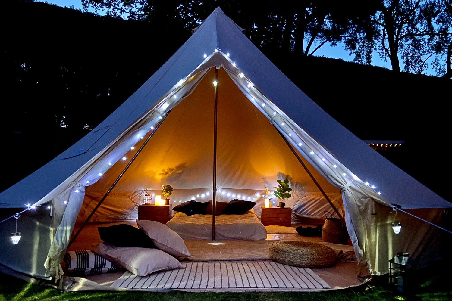 A bell tent glowing warm at night, the bed made up inside